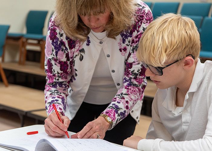 Woman in floral cardigan leans over a young person, pointing a pen at a paper. Immanuel Lutheran School | Belvidere, IL