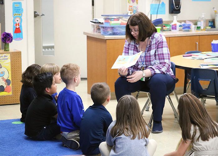 Teacher reading a story to a group of children seated on a blue rug in a classroom. Immanuel Lutheran School | Belvidere, IL