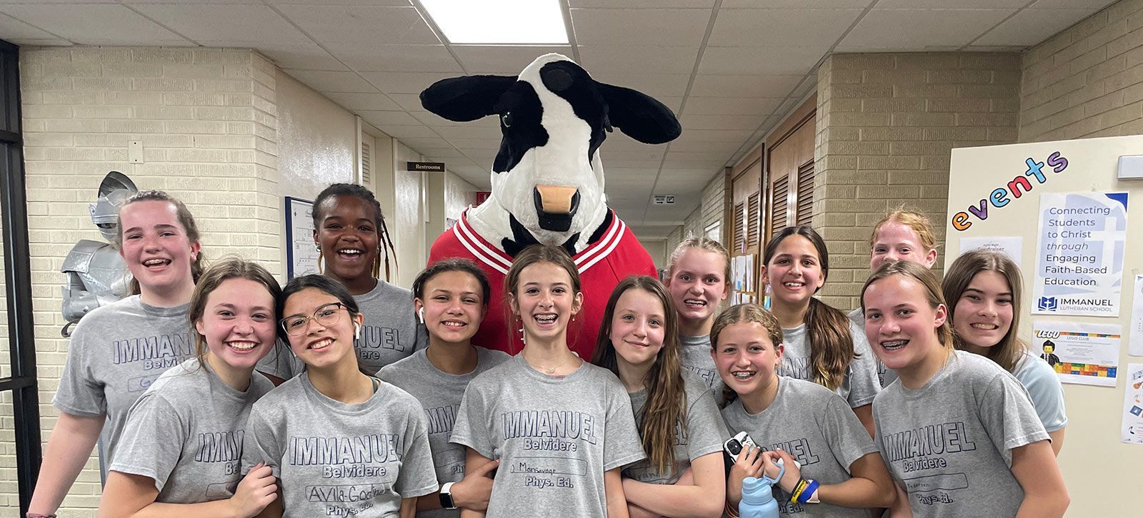 Group of smiling people pose with a cow mascot in a hallway. Middle School | Immanuel Lutheran School | Belvidere, IL
