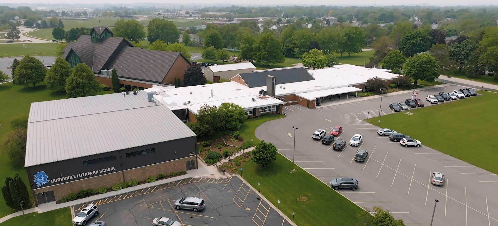 Aerial view of a church and building with multiple parking lots and cars. Extended Care | Immanuel Lutheran School | Belvidere, IL