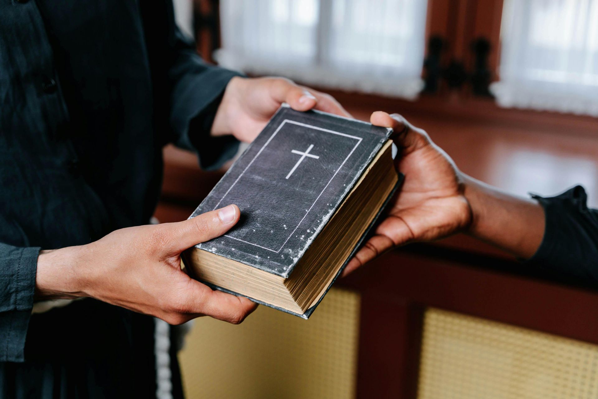 Hands passing a Bible with a cross on the cover. Discipleship | Immanuel Lutheran School | Belvidere, IL