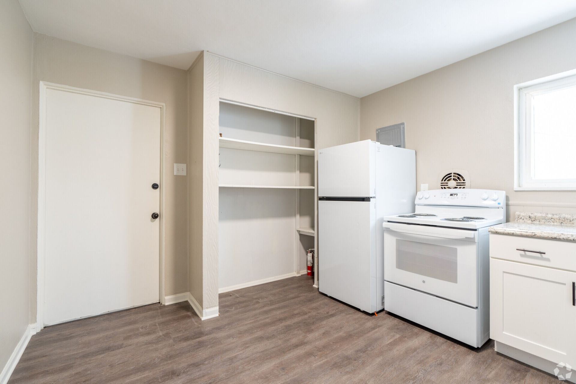 Empty kitchen/laundry room with white appliances, built-in shelves, and beige walls