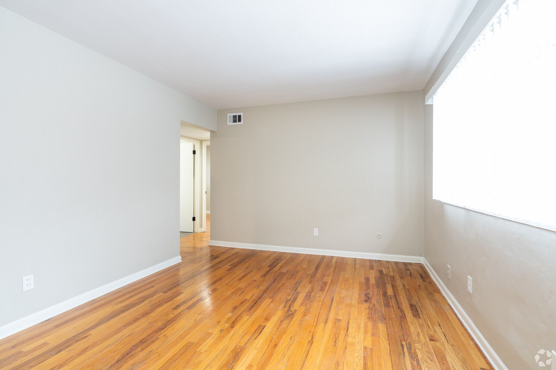 Empty room with hardwood floors, white walls, and a large window letting in daylight.