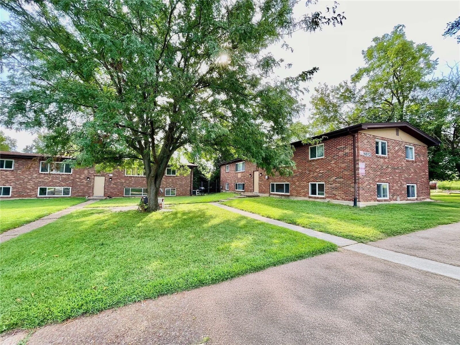 Apartment buildings around a grassy courtyard with large trees and a paved walkway
