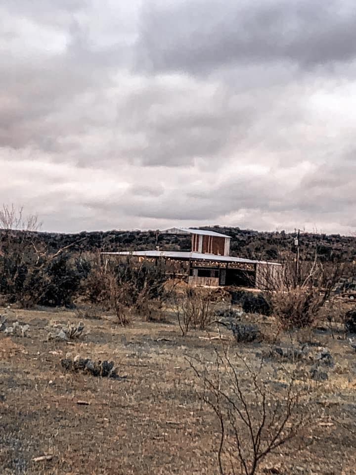 Dry scrubland with a small modern house under a cloudy sky, seen in the distance