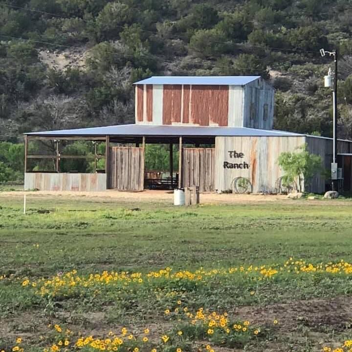 Rustic ranch building with weathered metal siding in a grassy field beneath hills