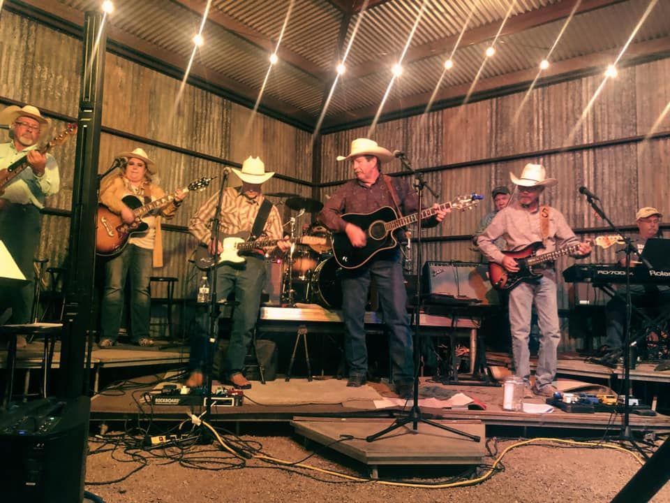 Country band performing on a rustic stage under warm string lights, with guitars and keyboard.