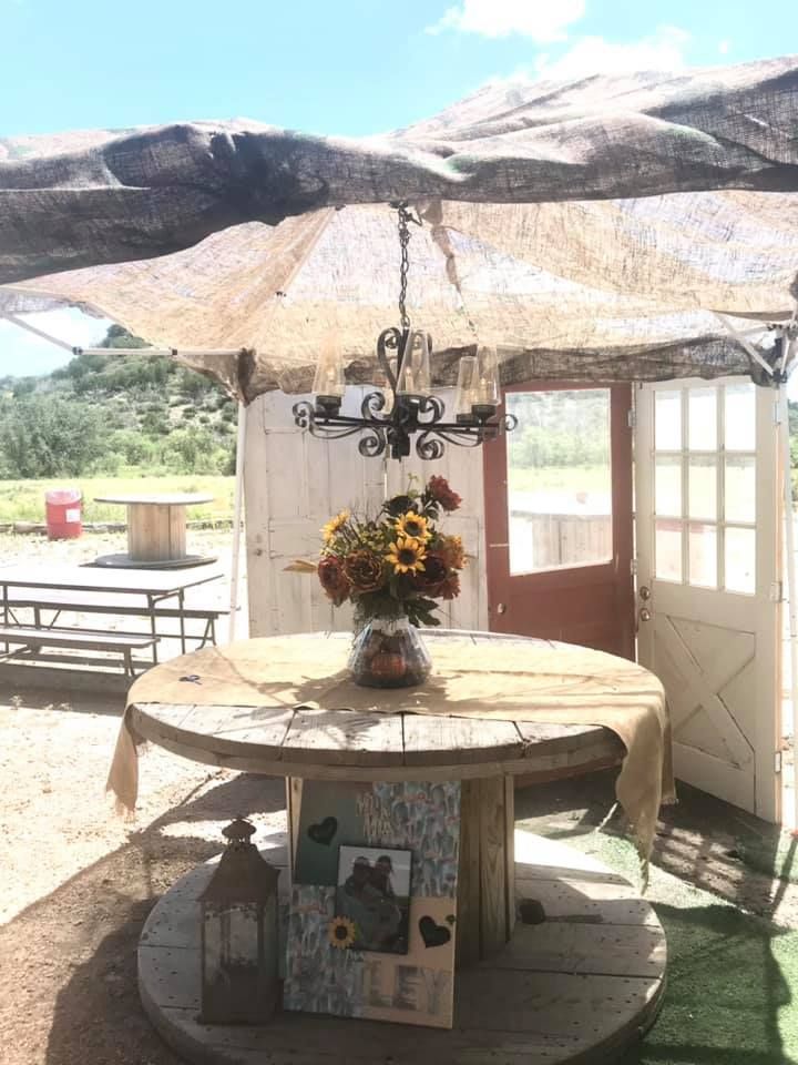 Round rustic table under a patio umbrella with a flower vase, in a sunny outdoor garden setting