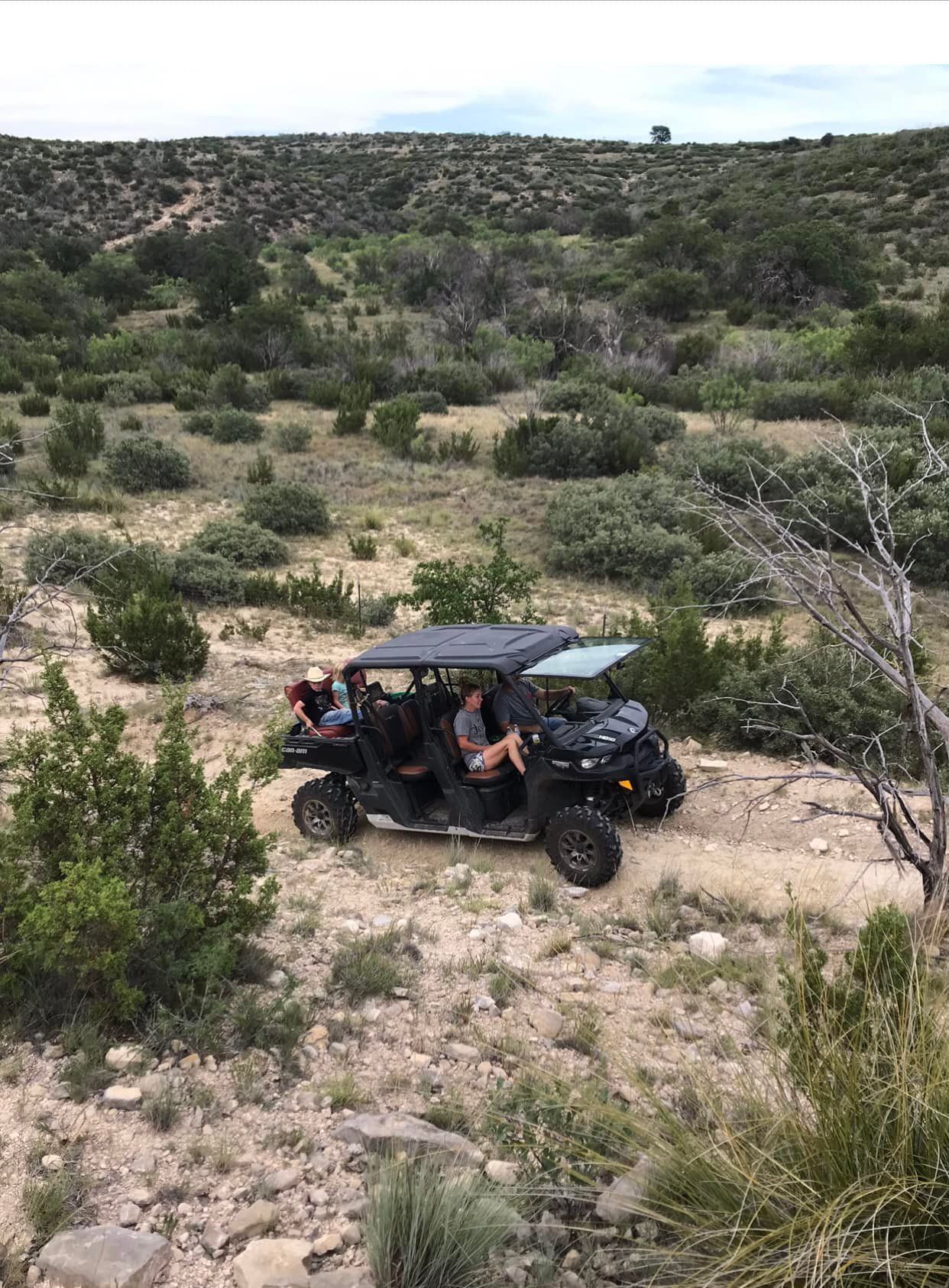 Off-road utility vehicle with passengers driving on a rocky desert trail amid low shrubs