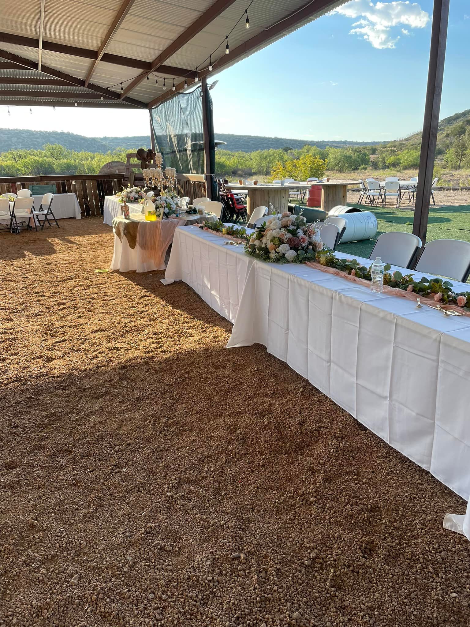 Outdoor buffet table under a canopy at a scenic event venue, with white tablecloths and food displays.