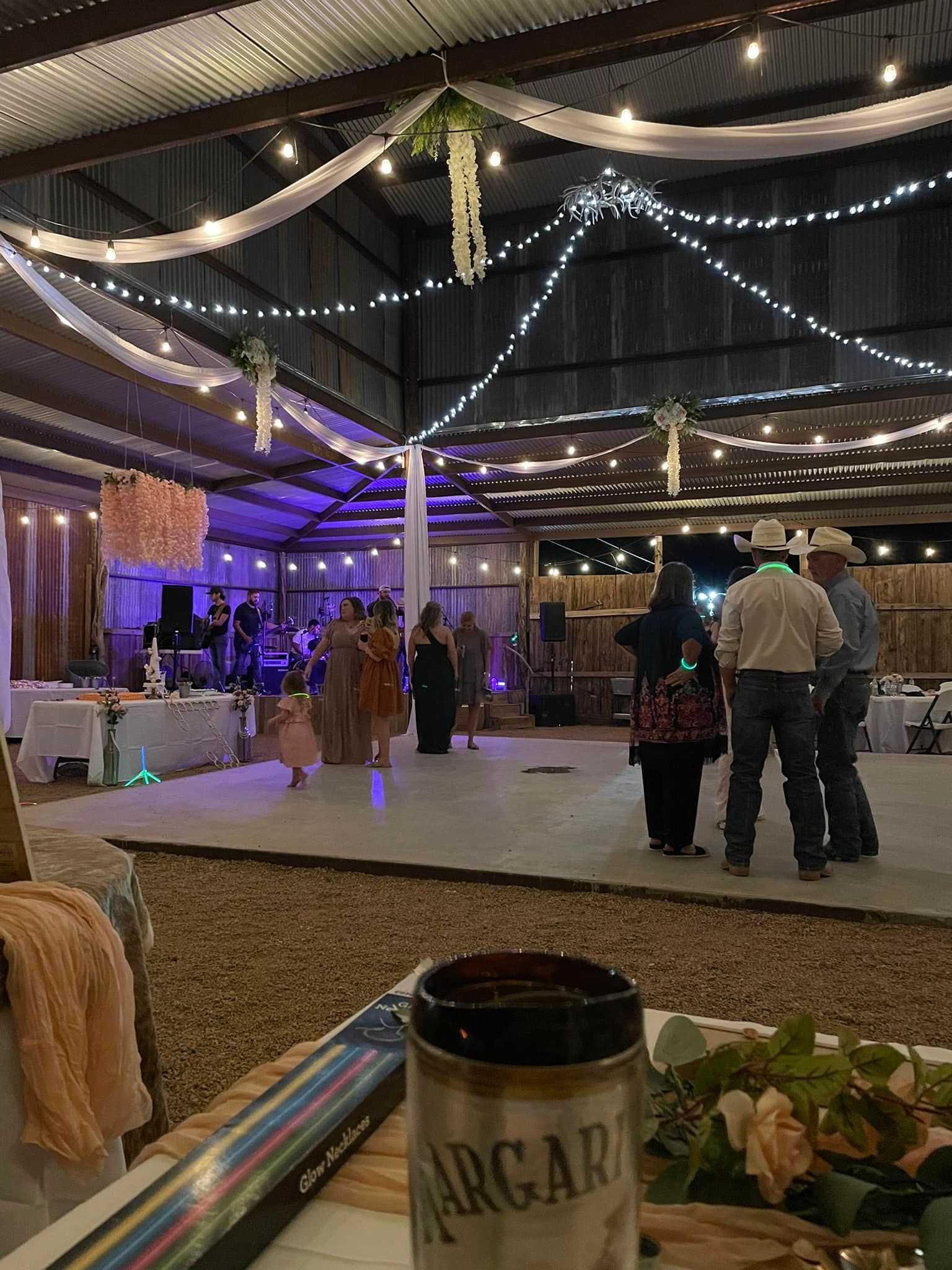 Indoor party venue with purple lights, draped ceiling decor, and guests standing near tables.