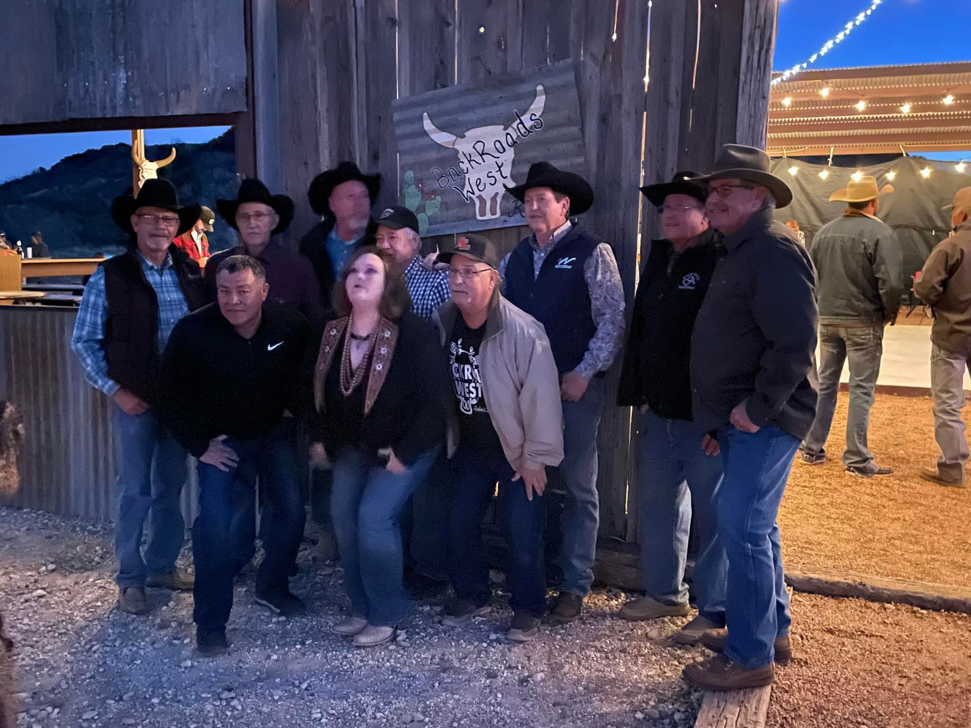 Group of people posing outdoors at night under string lights beside a rustic barn.