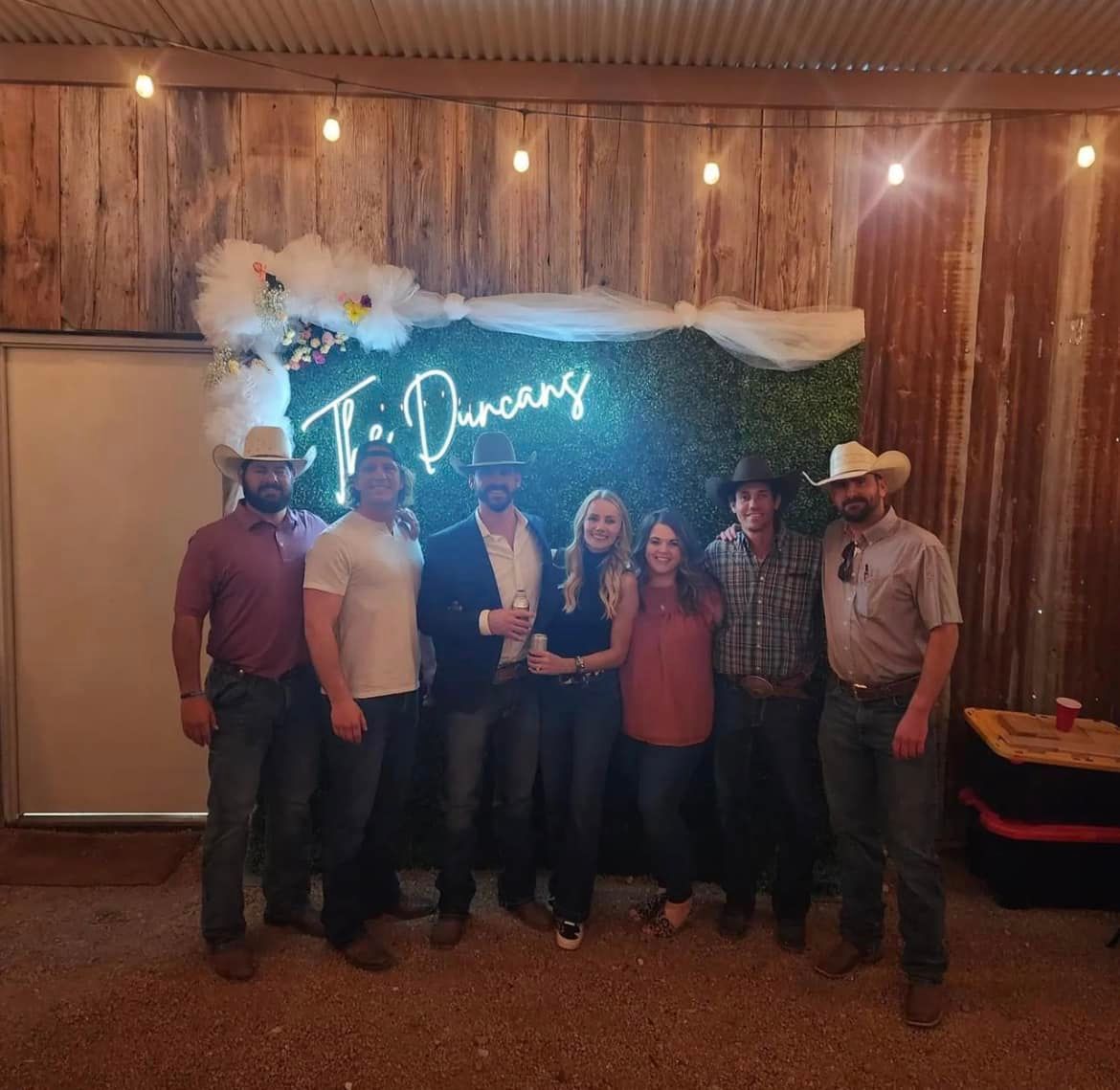 Group posing indoors at a rustic event venue with a neon “Dreams” sign and string lights.