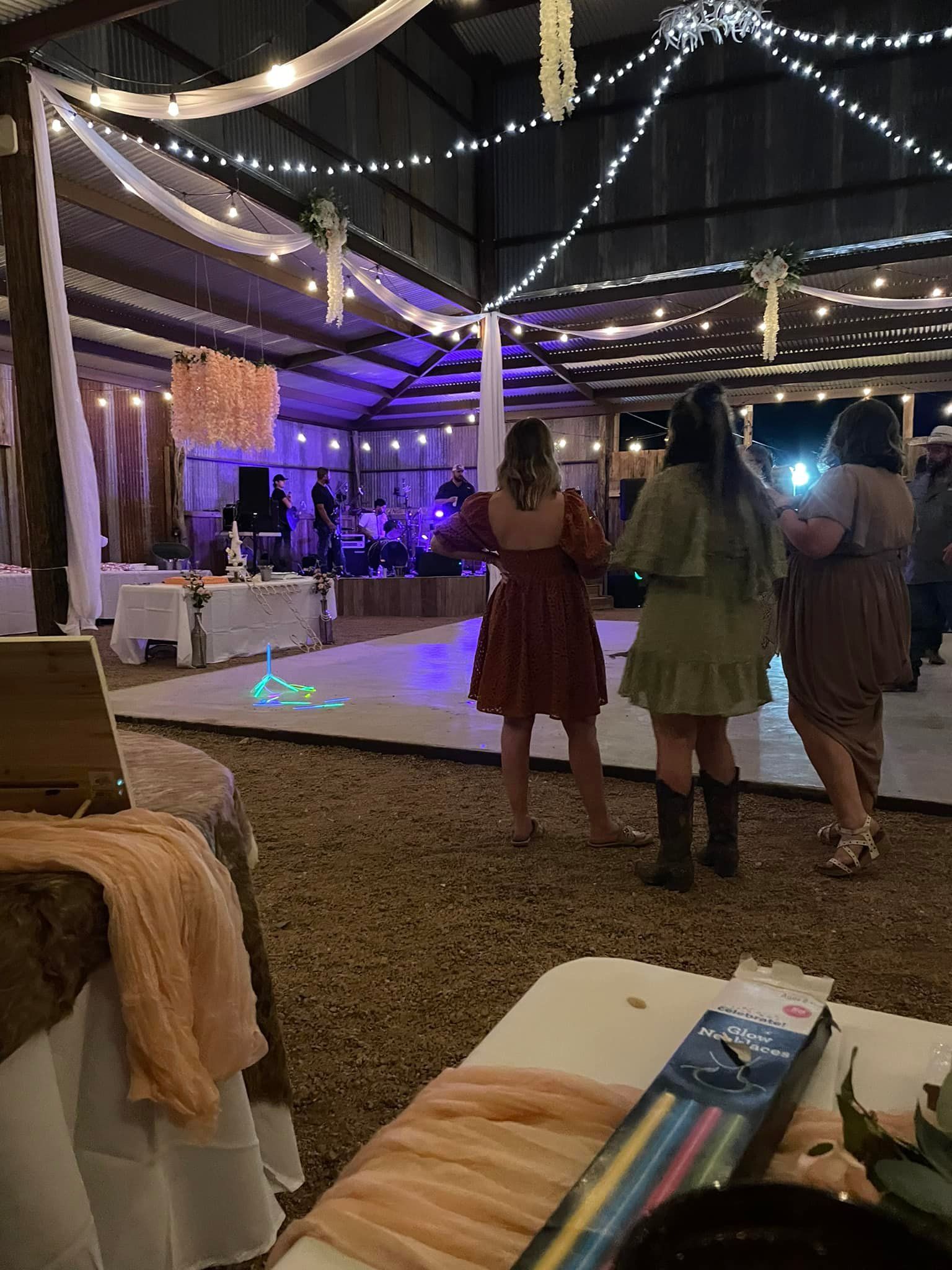 Three people standing at a lit outdoor event with string lights and a dance floor at night
