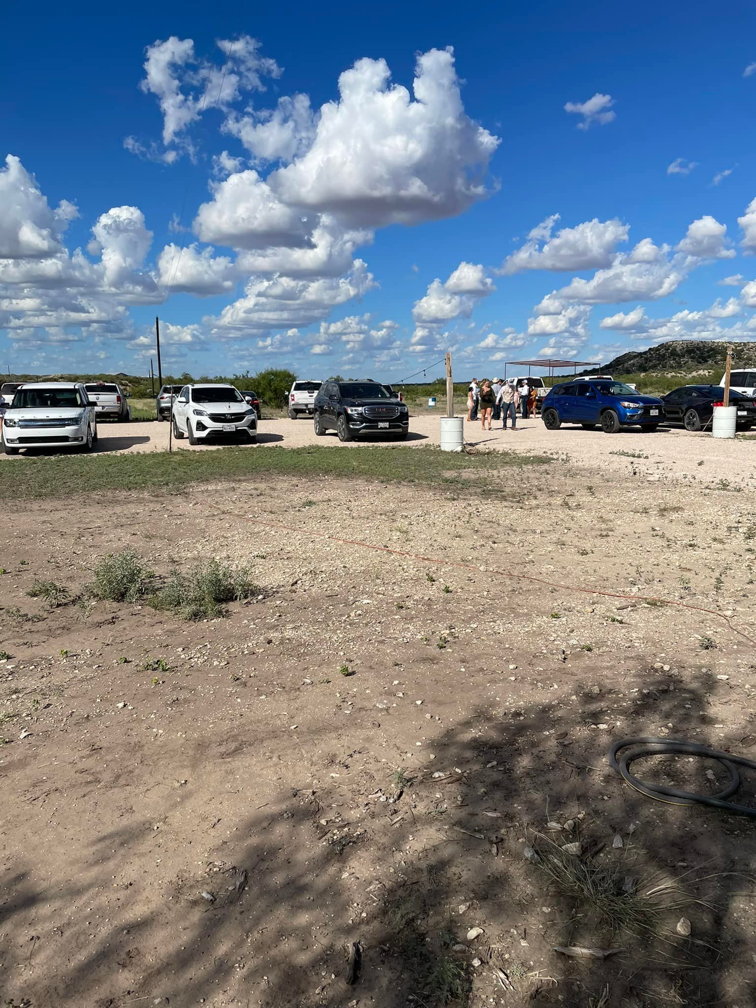 Gravel lot with parked trucks under a bright blue sky with large white clouds and a few people in the distance