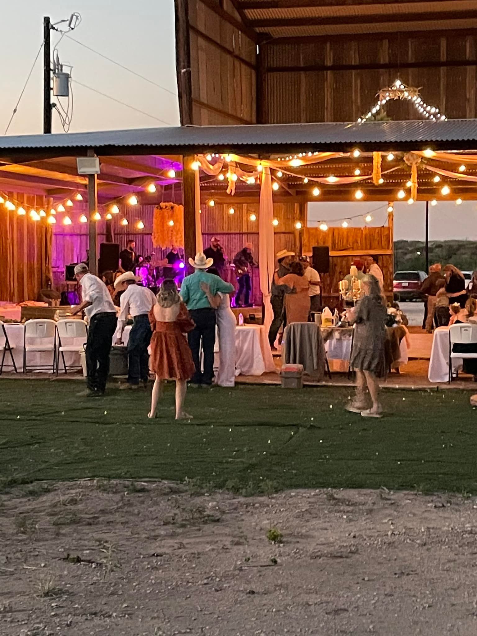 Outdoor evening gathering under string lights with people mingling on a lawn beside a lit tented venue