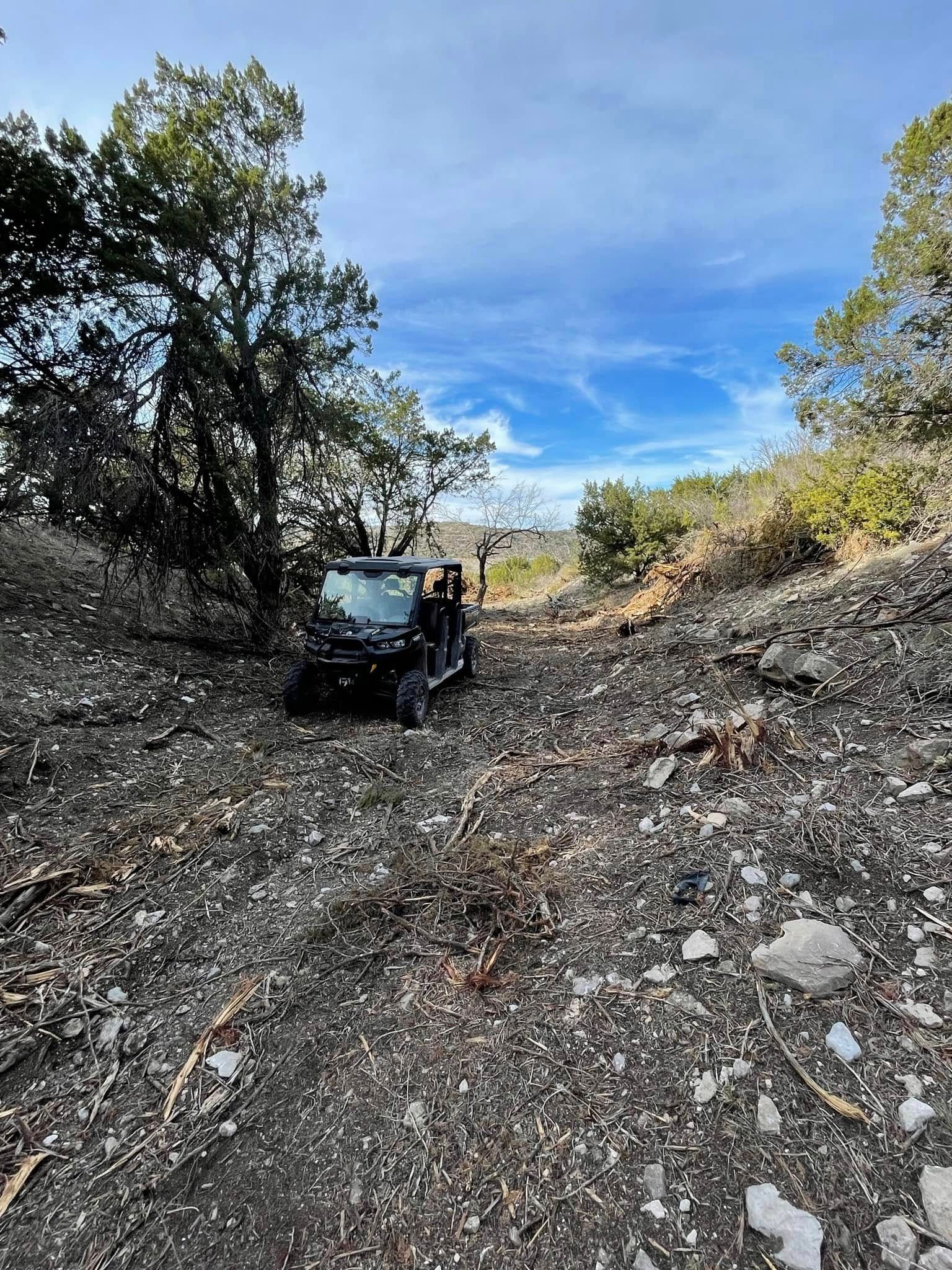 Black off-road vehicle on a rocky dirt trail between trees under a blue sky.