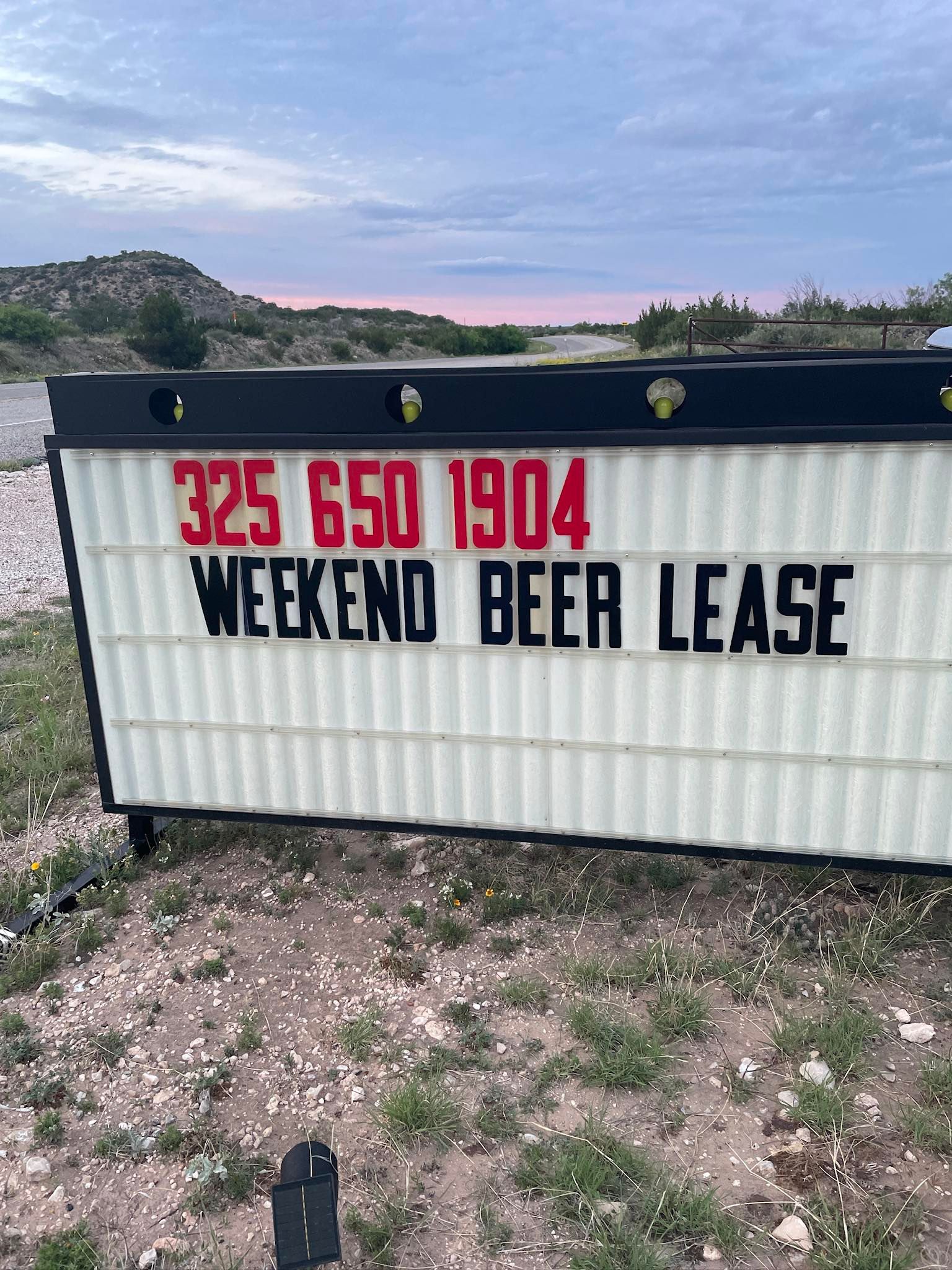 Sign for weekend beer lease with red phone number on a white board outdoors at dusk