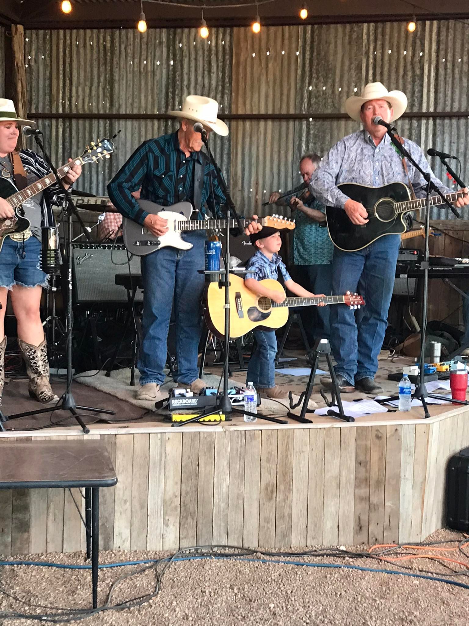 Country band performing on a wooden stage with guitars and cowboy hats under string lights
