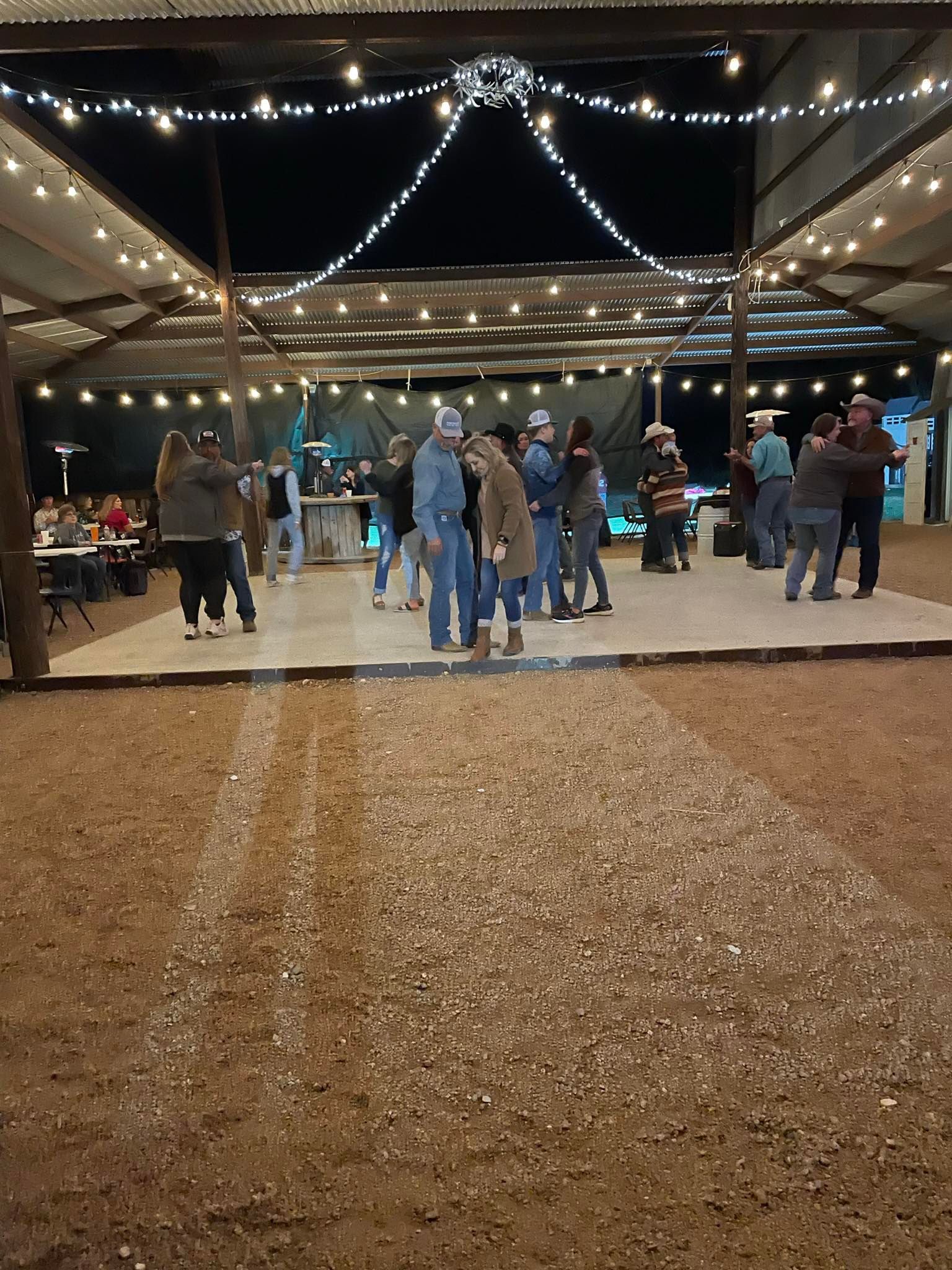 People mingling under string lights at a nighttime outdoor event on a gravel patio