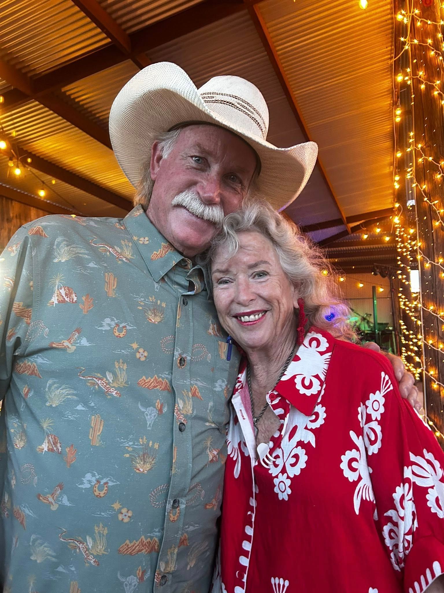 Smiling couple in cowboy hats and western shirts posing under warm lights