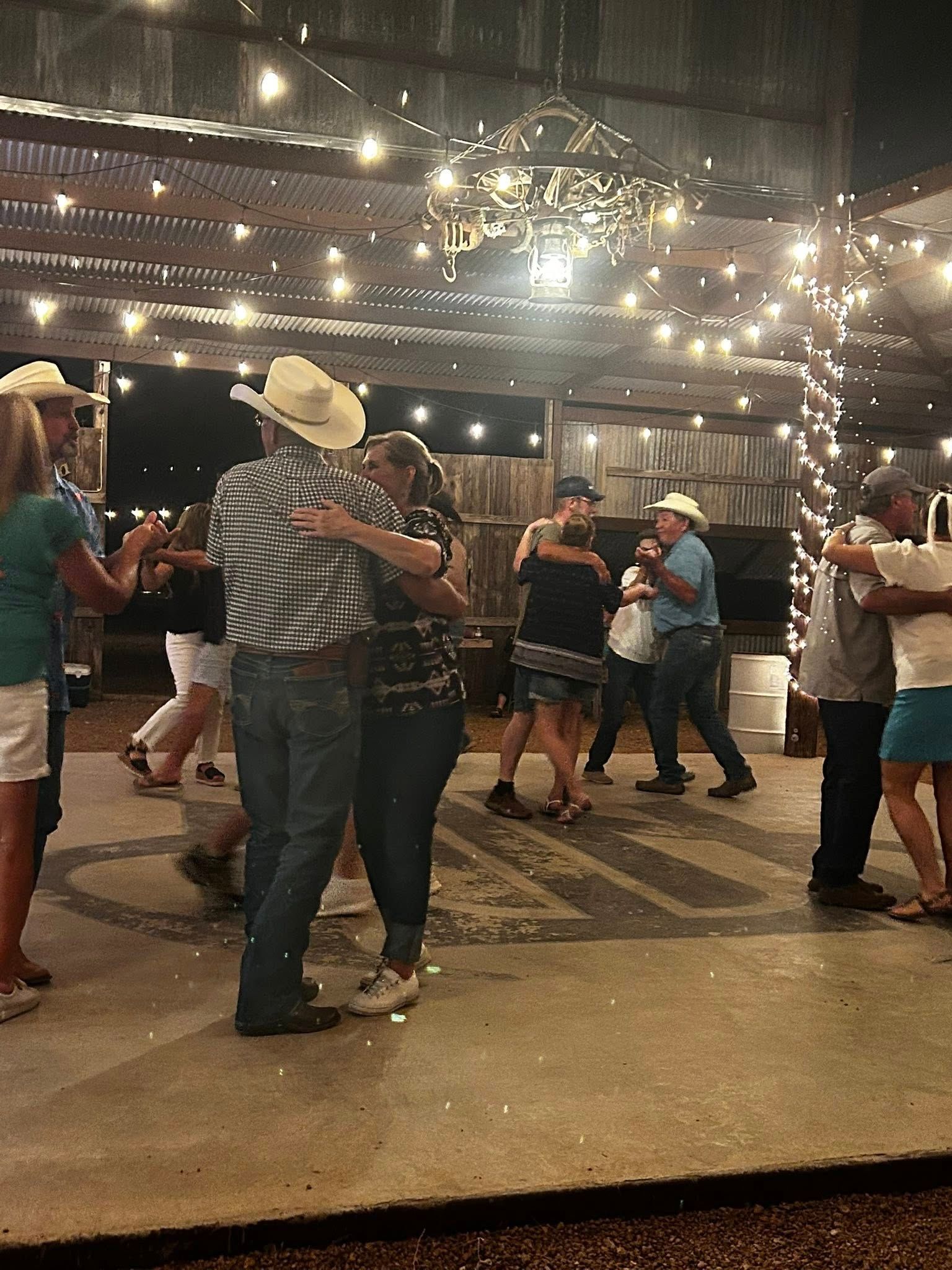 People dancing at a nighttime outdoor party under string lights, with a chandelier overhead.