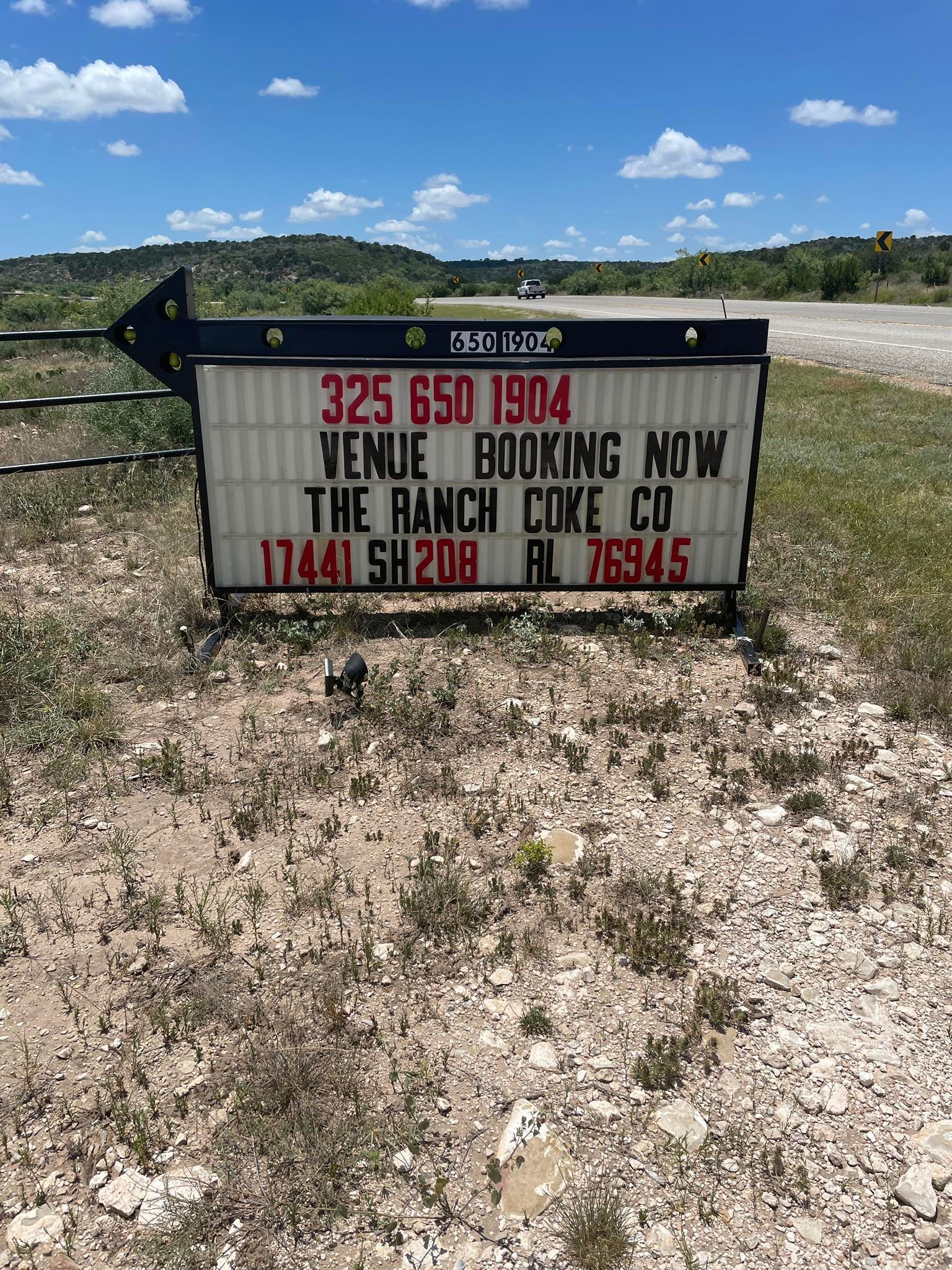 Sign for The Ranch Coke Co. in a grassy field with mountains in the distance.