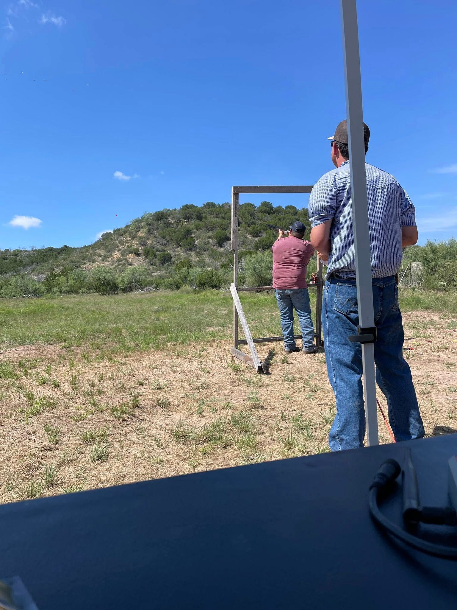 People standing at an outdoor shooting range under a bright blue sky