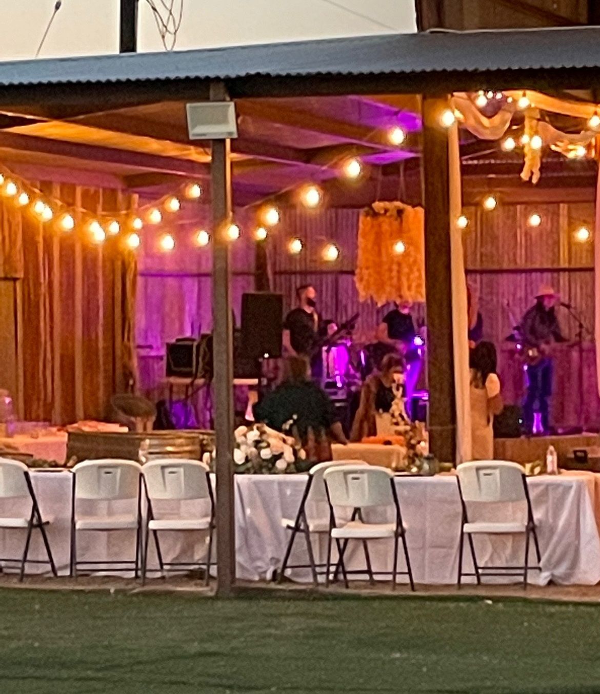 Outdoor evening event with string lights, seated guests, and a purple-lit live band on stage