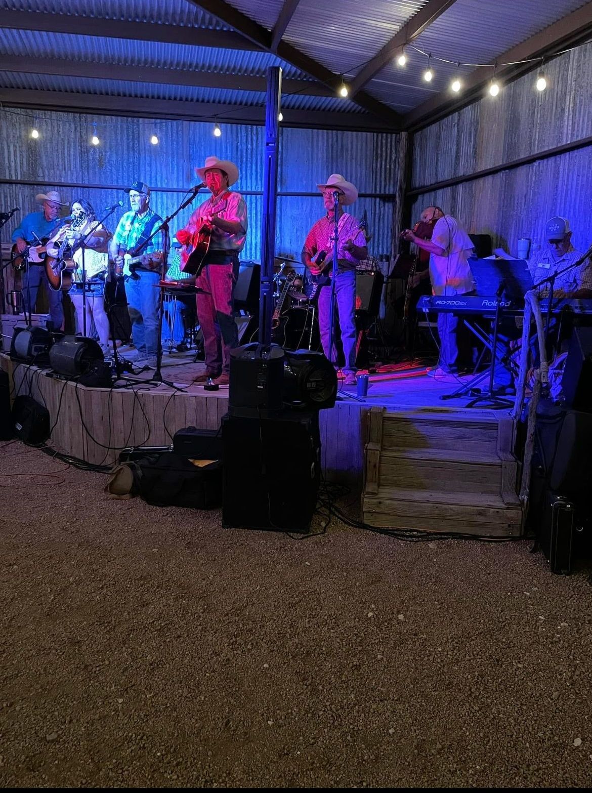 Live band performing on an outdoor stage under blue and purple lights at night