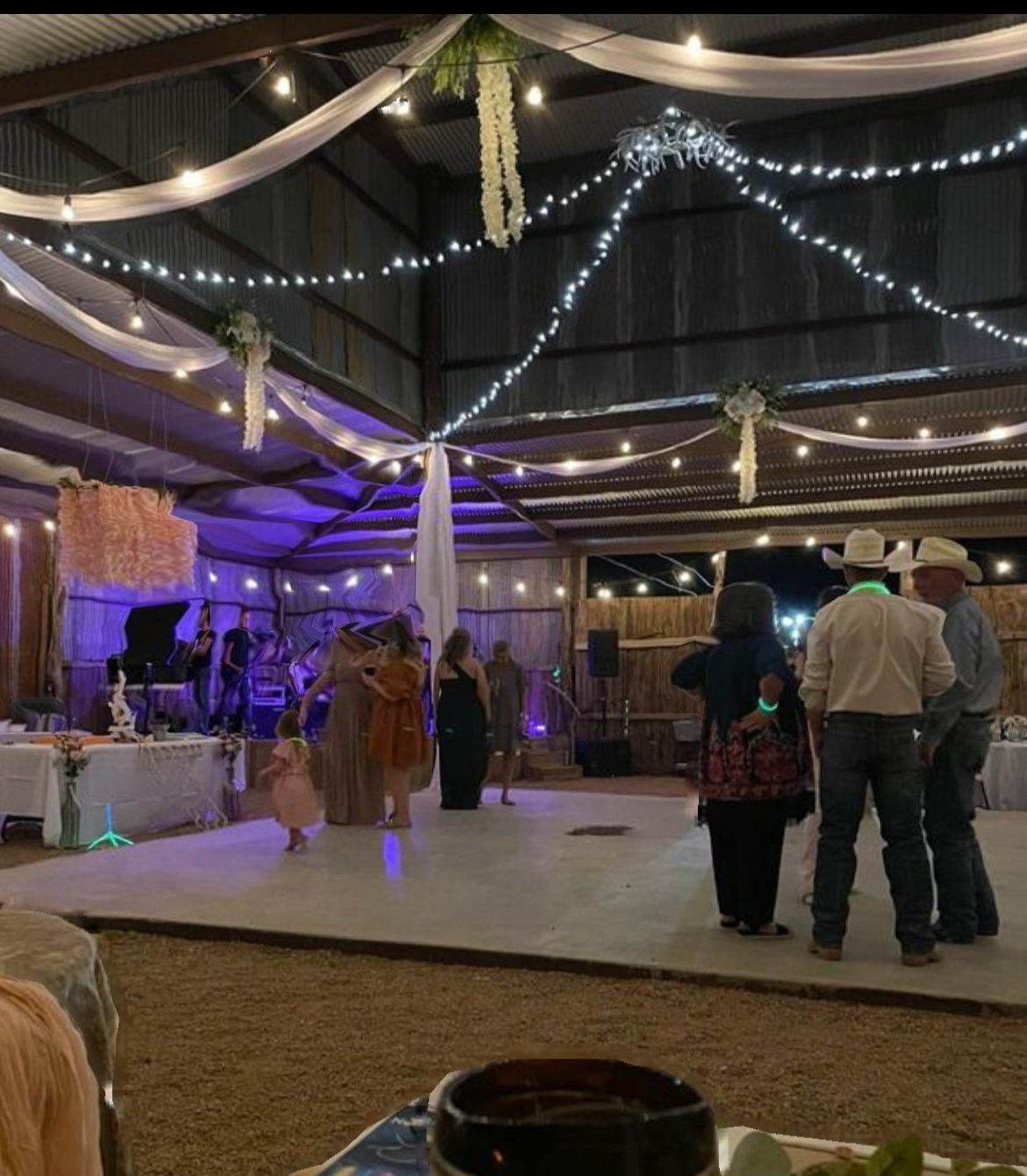 Indoor event hall with string lights, a stage, and guests mingling on a dance floor under draped fabric.