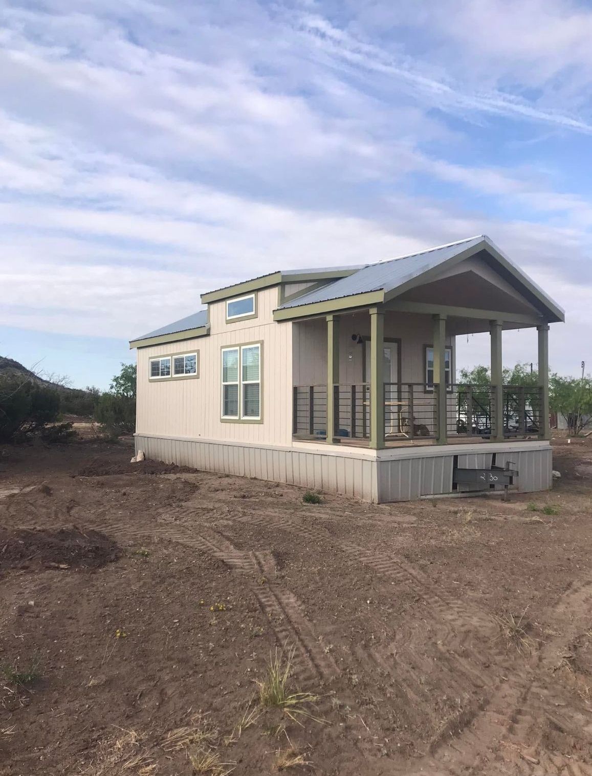Small beige house with a covered porch on a barren lot under a cloudy sky