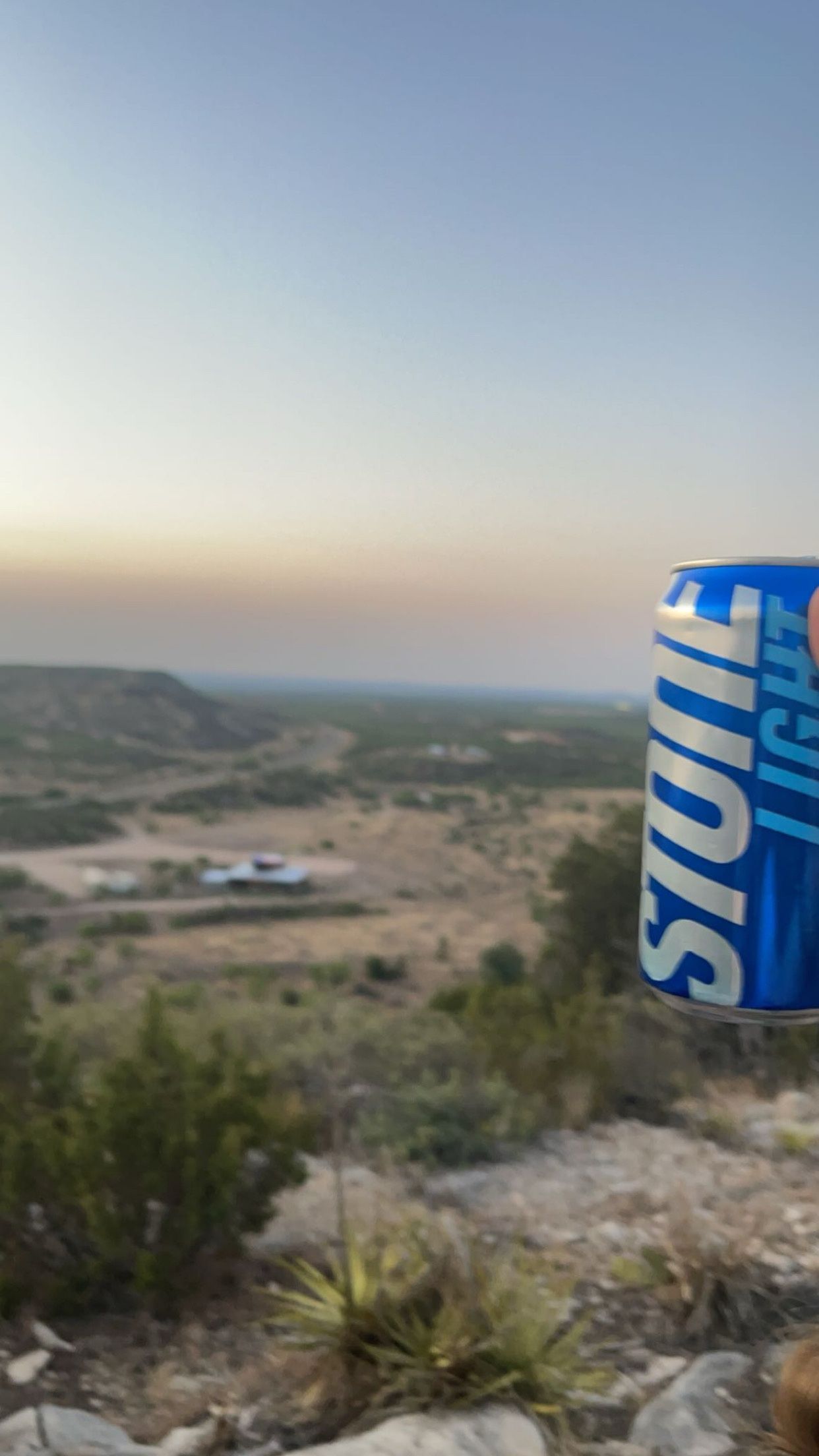 Blue can on a rocky hillside overlooking a valley at sunset