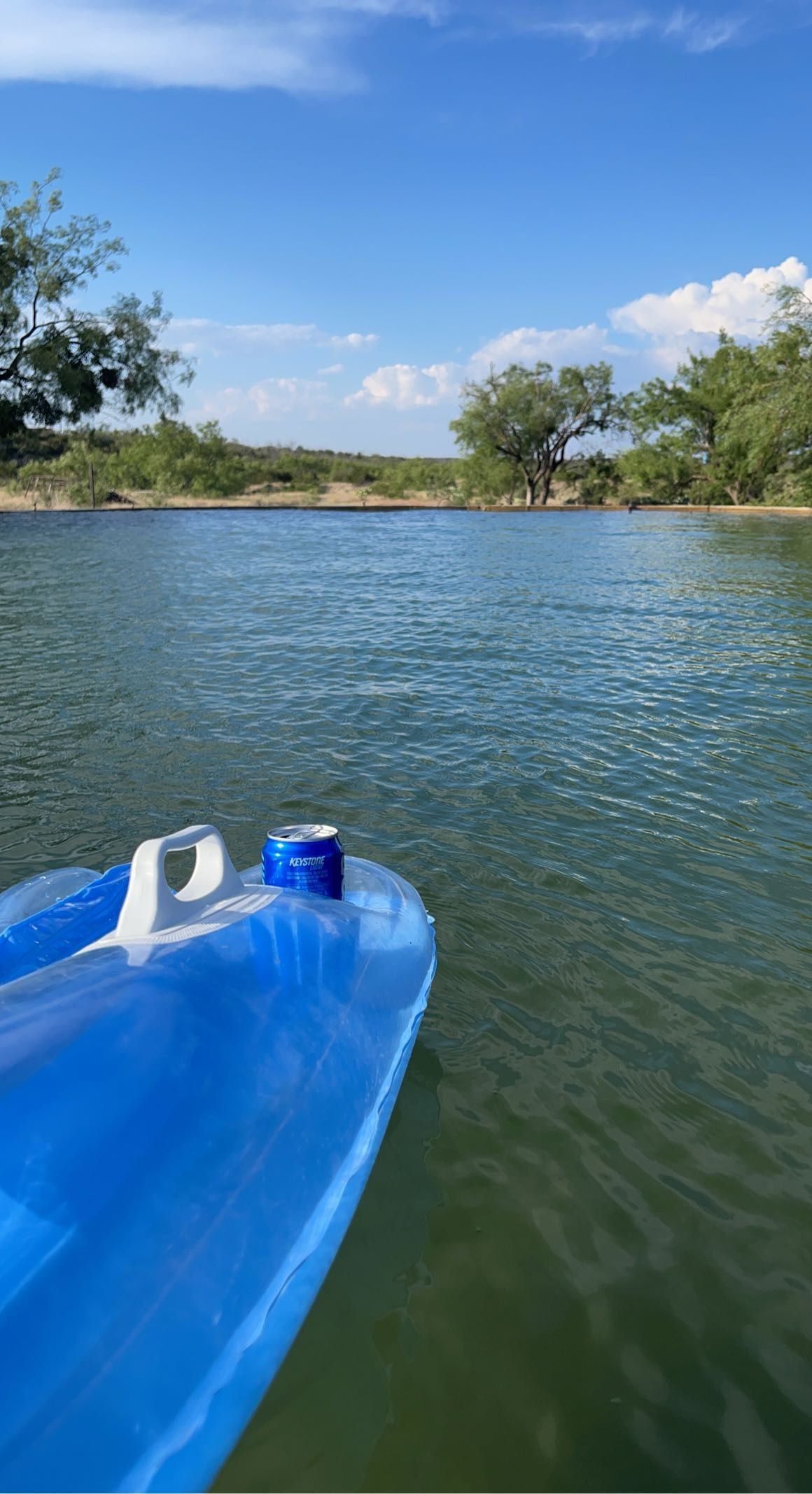 Blue kayak on calm water under a clear sky, with trees lining the distant shore.