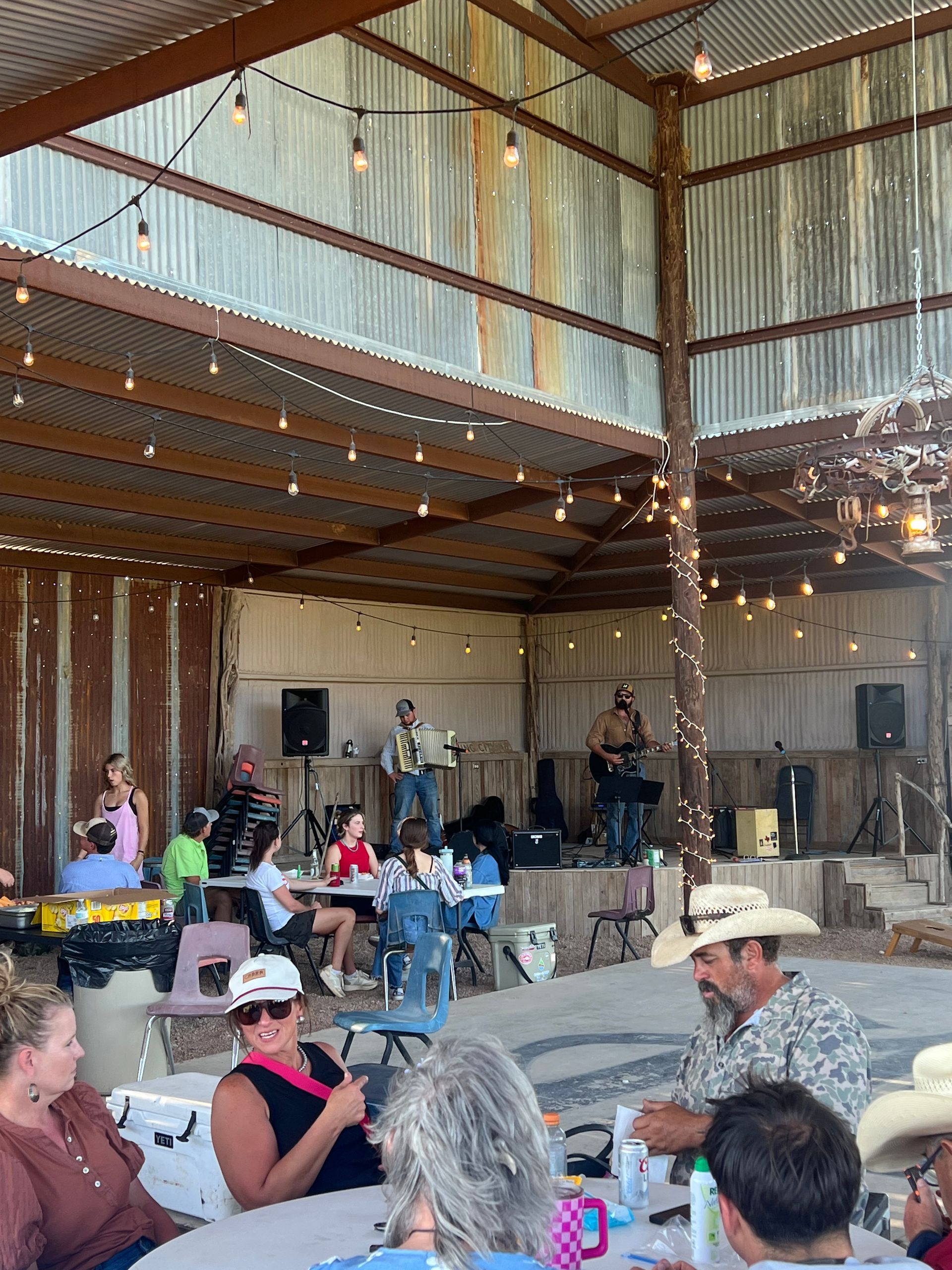 Indoor barn-style live music performance with seated audience and string lights.