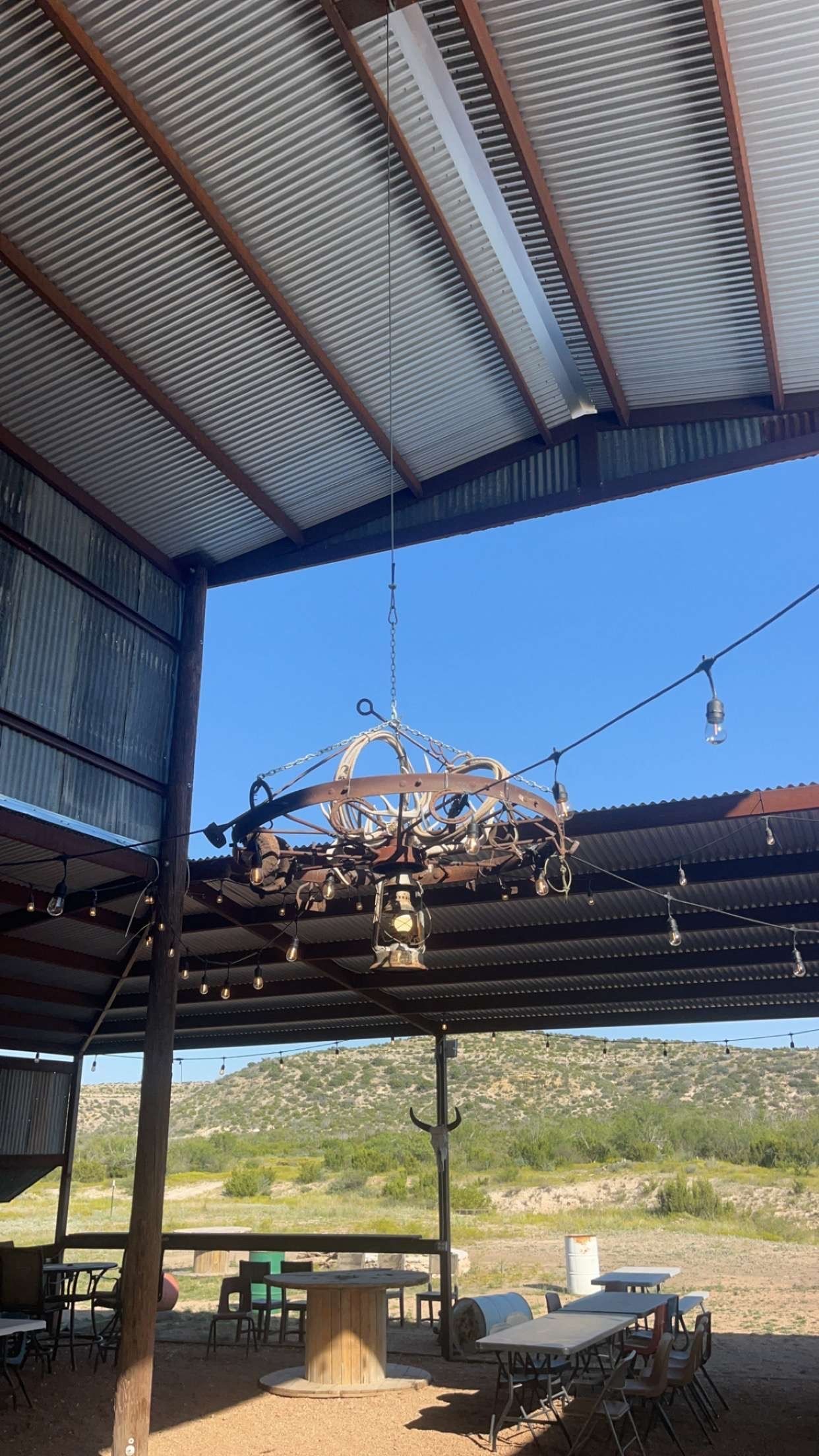 Open-air patio with metal roof, hanging dried plants, and a view of fields beyond.