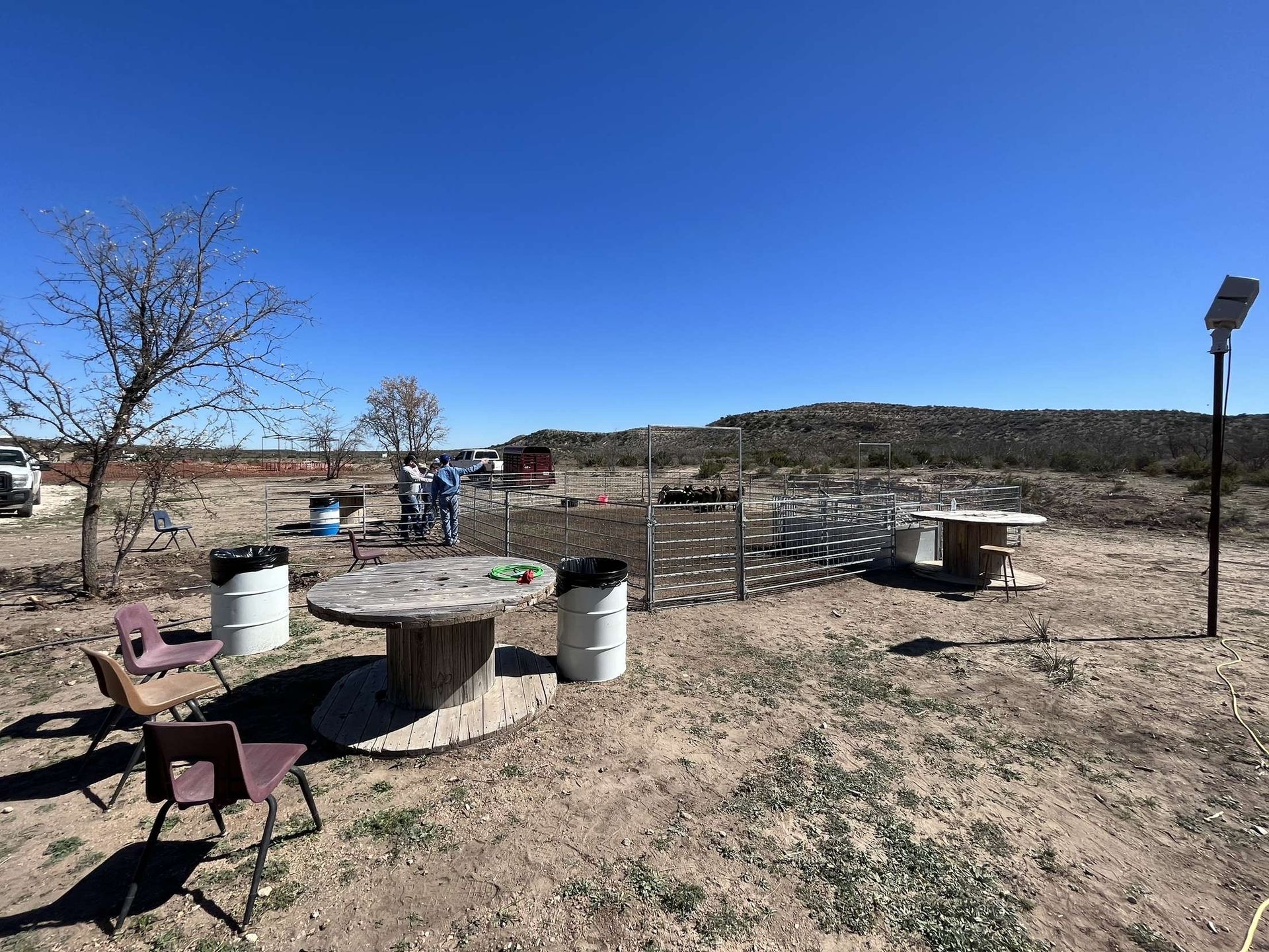 Desert picnic area with concrete tables, metal grills, a fence, and a clear blue sky.