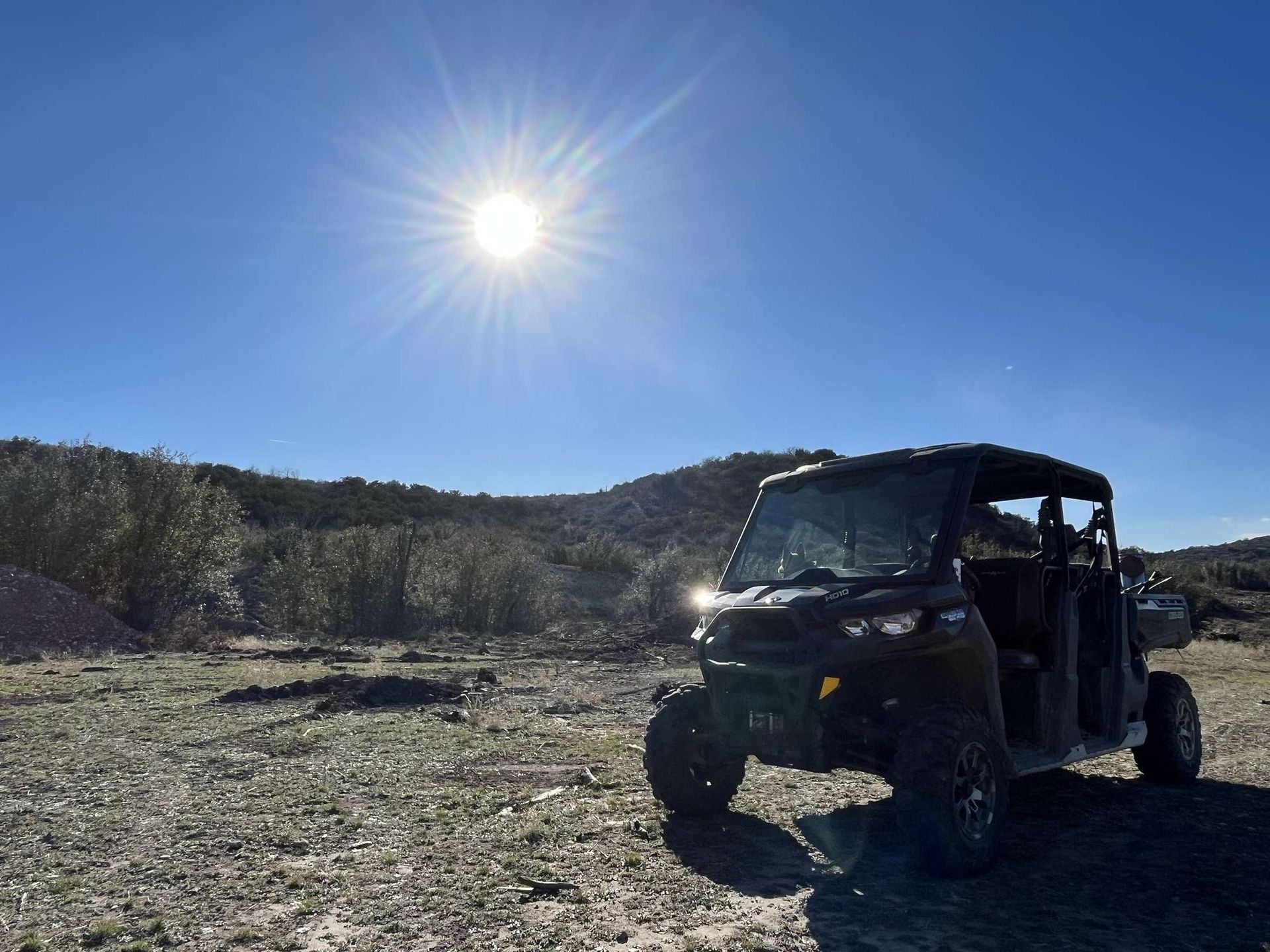 Off-road utility vehicle on a rocky trail under a bright sun with trees in the background