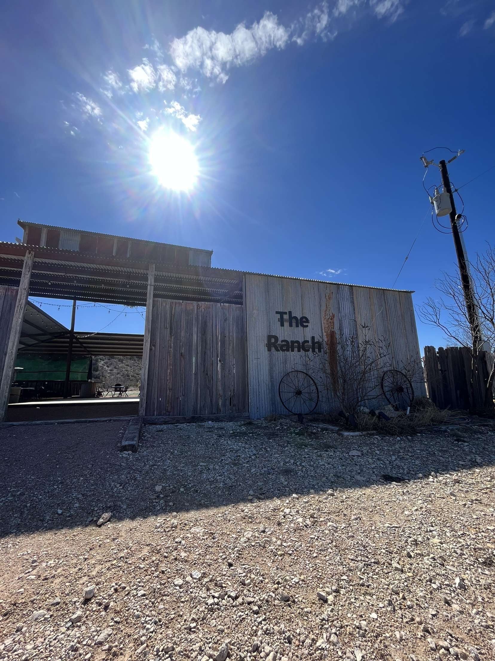 Sunlit rustic wooden building with faded sign beside a gravel lot under a bright blue sky
