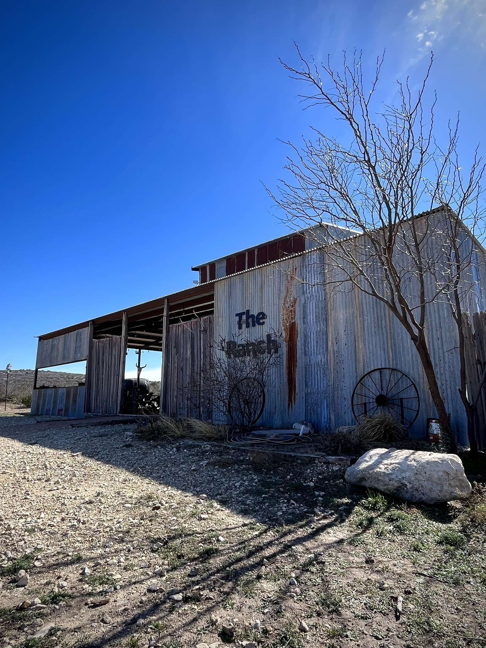 Old weathered barn with a metal roof in a dry field under a clear blue sky