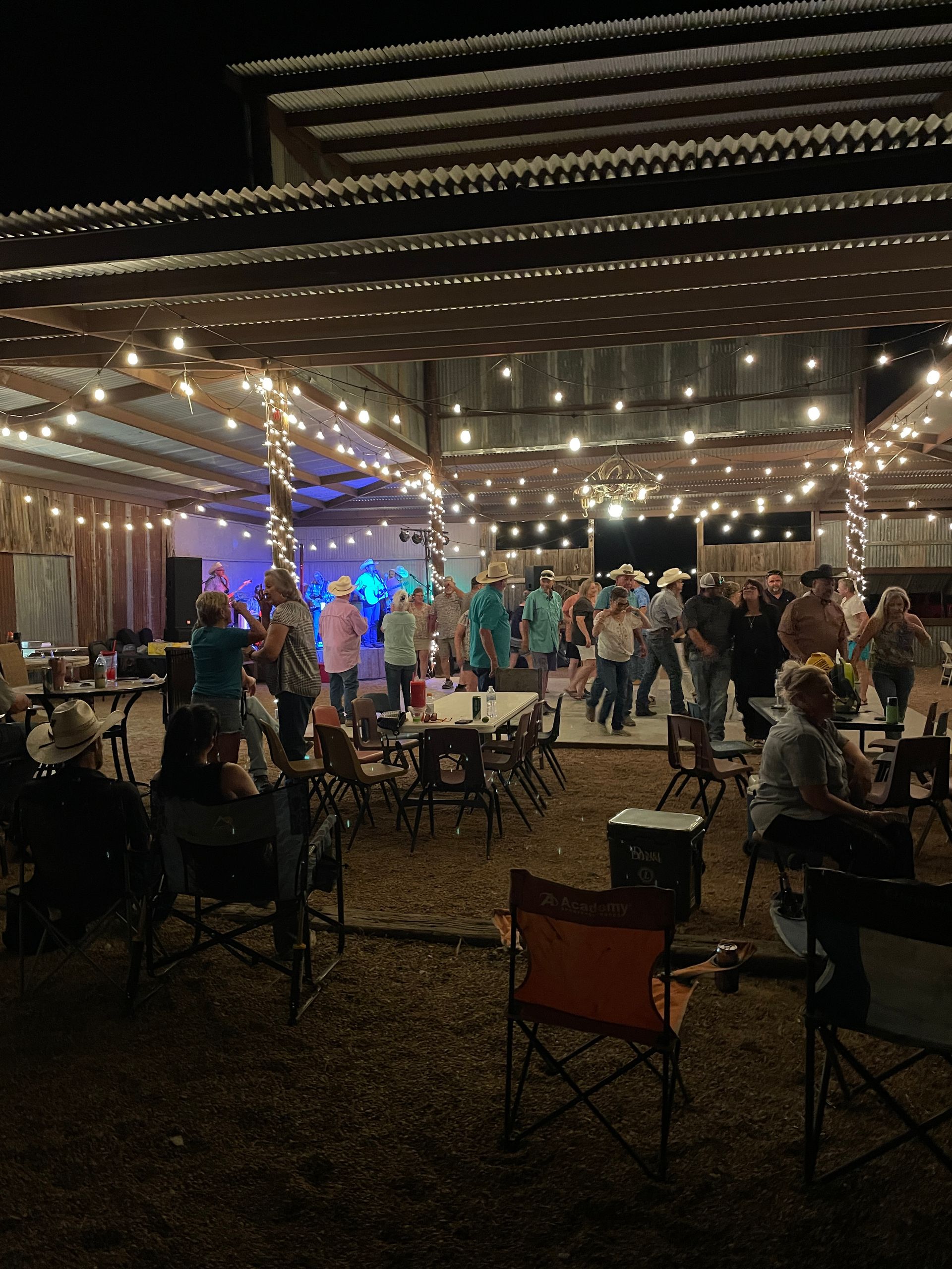 Outdoor nighttime event with string lights, seated guests, and people dancing near a lit stage