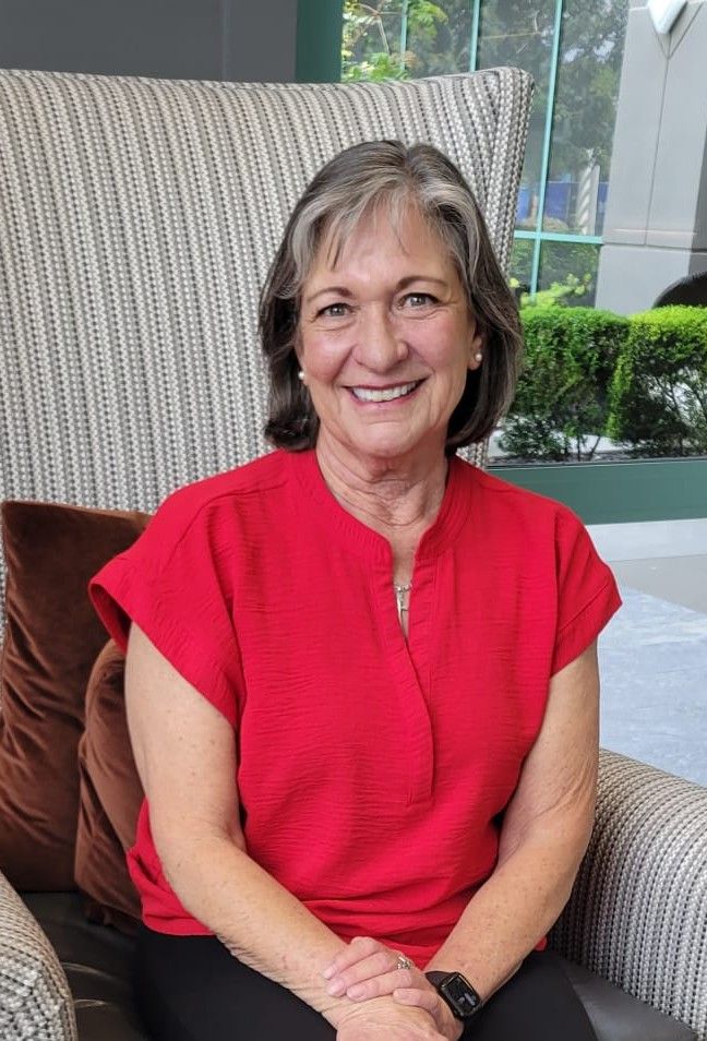 Woman with short, graying hair smiles, wearing a burgundy top, in front of a neutral wall.