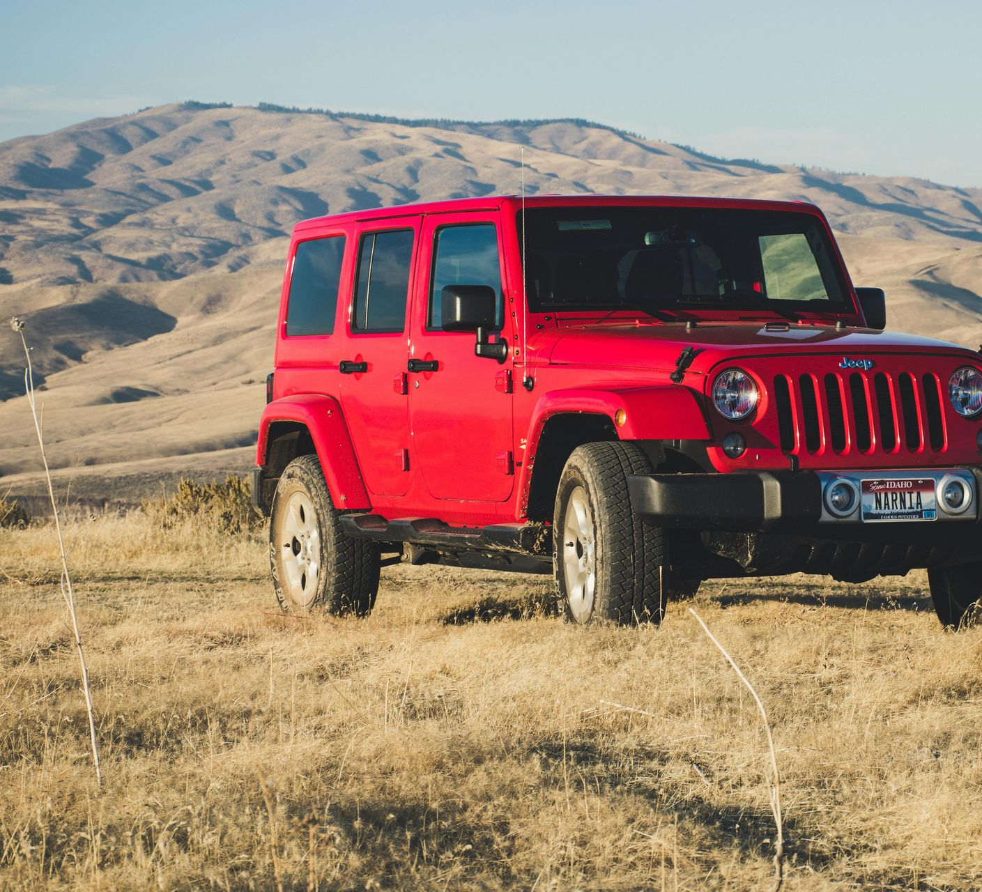 Red Jeep parked on a grassy hilltop overlooking a mountain range.