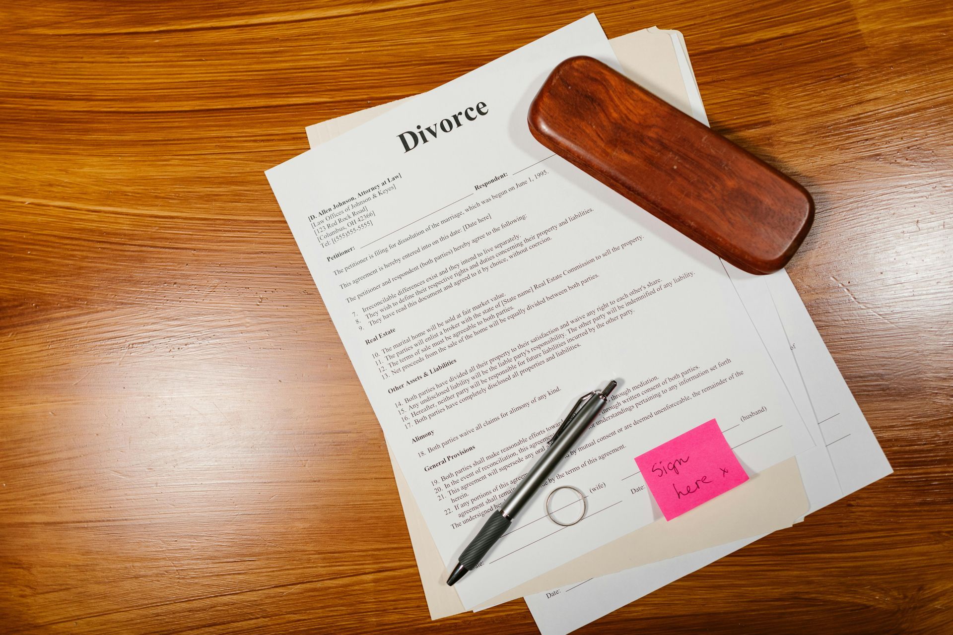 Divorce document on a wooden desk with a pen, stamps, and a pink sticky note.