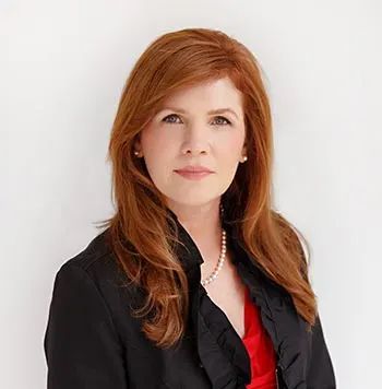 Portrait of a woman with red hair in a black blazer and red top against a white background