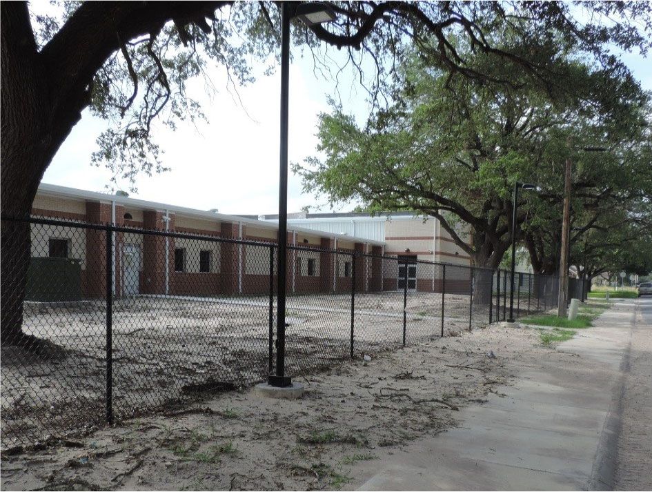 A chain link fence surrounds a large brick building