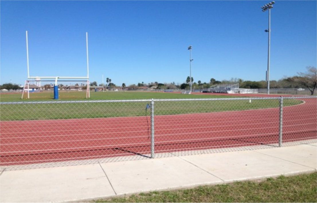 A running track with a fence around it and a football field in the background.