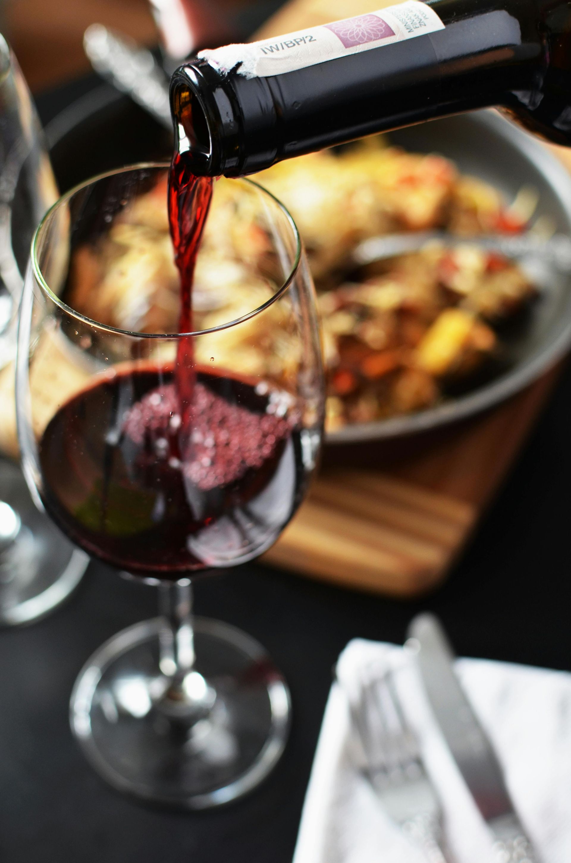 A glass of red wine is being poured from a bottle