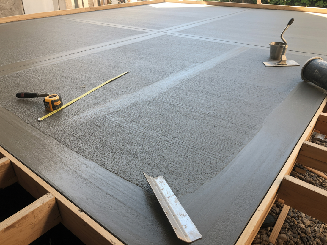 Fresh gray concrete floor being smoothed with tools on a construction site