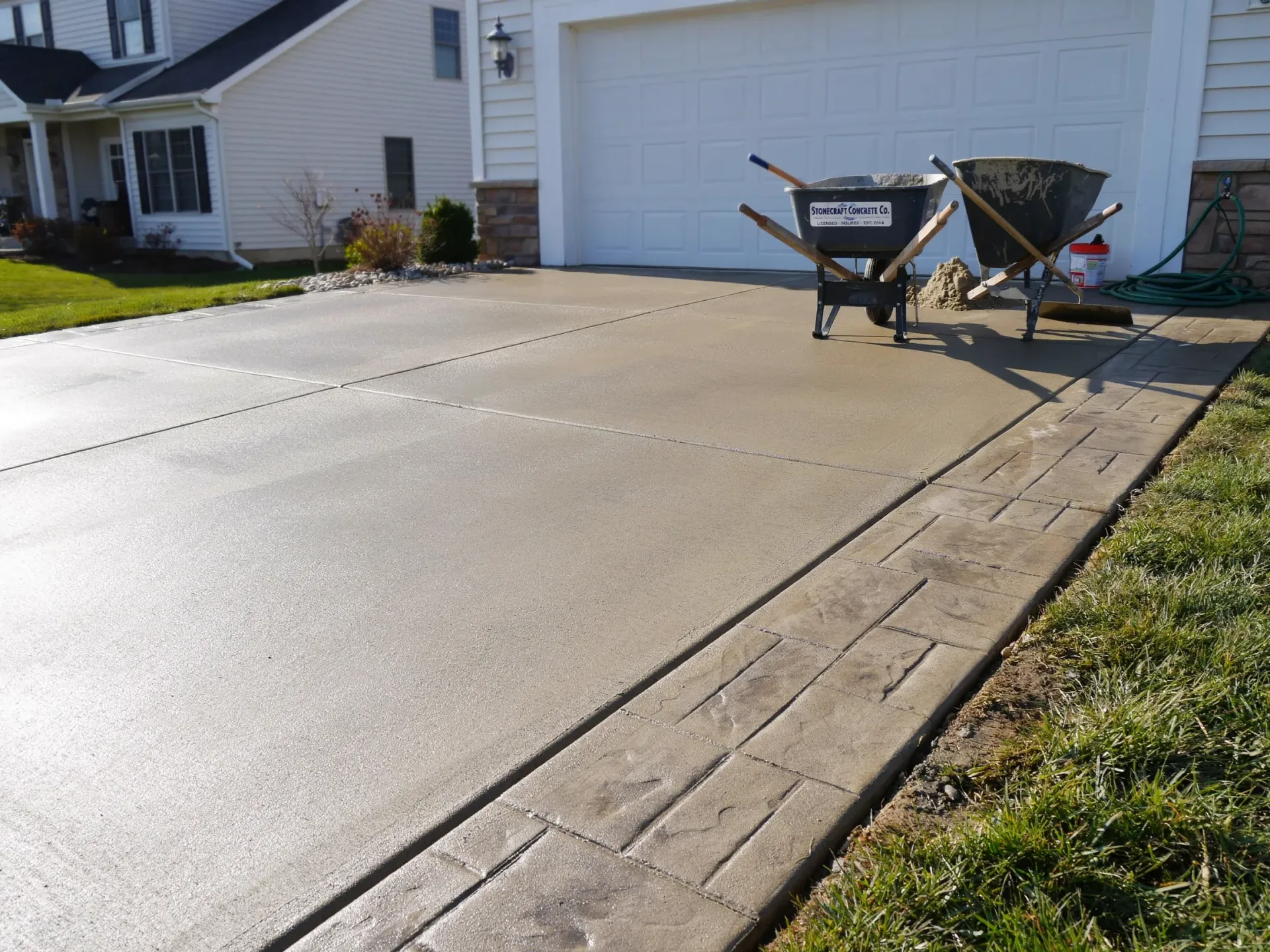 Concrete driveway in front of a garage with two wheelbarrows and a hose on the right side